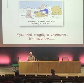 Mann foran forsamling. På presentasjons-sliden står det "If you think integrity is expensive, try misconduct"