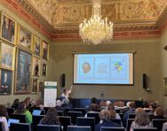 Helene Ingierd raises her arm to a presentation on a board in a grand room with a noticable chandelier.