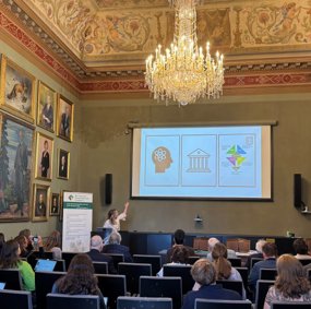 Helene Ingierd raises her arm to a presentation on a board in a grand room with a noticable chandelier.