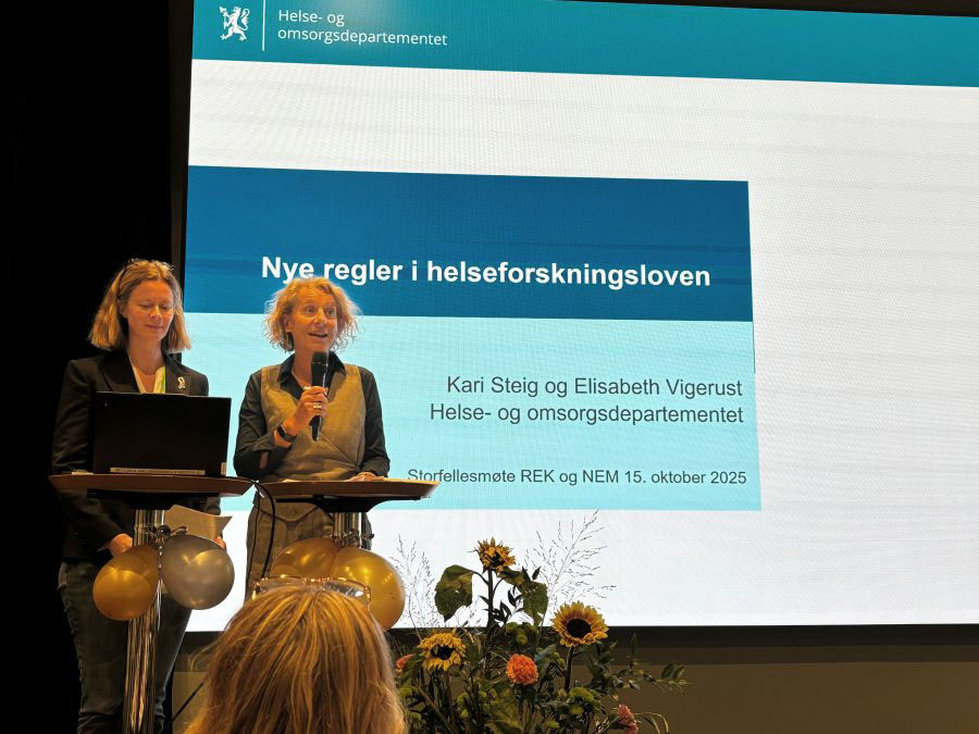 Kari Steig og Elisabeth Vigerust står på en talerstol. De viser en presentasjon der det står "nye regler i helseforskningsloven".