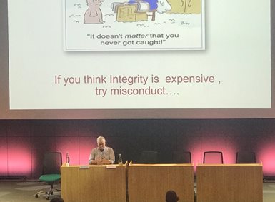 Mann foran forsamling. På presentasjons-sliden står det "If you think integrity is expensive, try misconduct"
