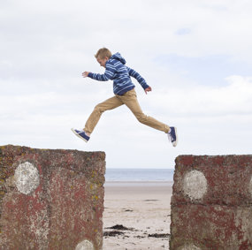 Gutt som hopper over fra en del av en mur til en annen.