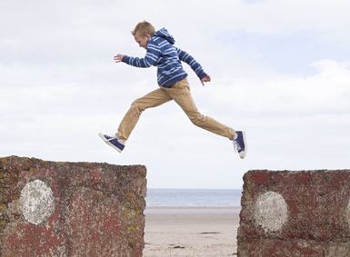 Gutt som hopper over fra en del av en mur til en annen.