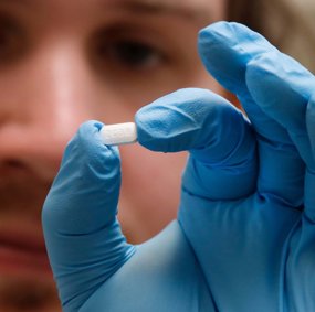 En person med blå plasthanske held ei pille