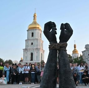 En folkemengde står rundt en skulptur av to bundne hender som strekkes mot himmelen.